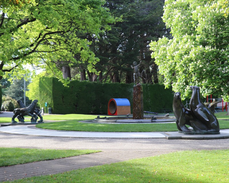Large trees surround a fountain with statues of animals and a small Peter Pan on a column.