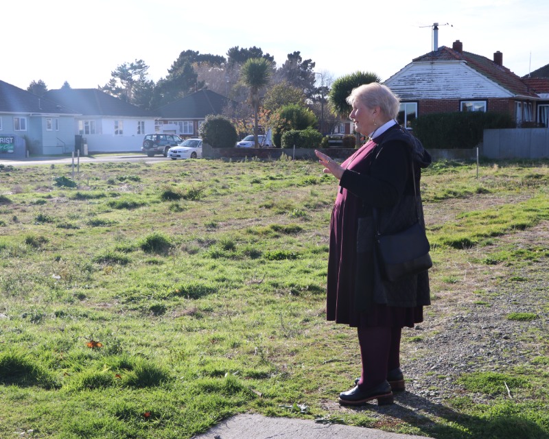 A person standing in a grassy section with houses in the background.