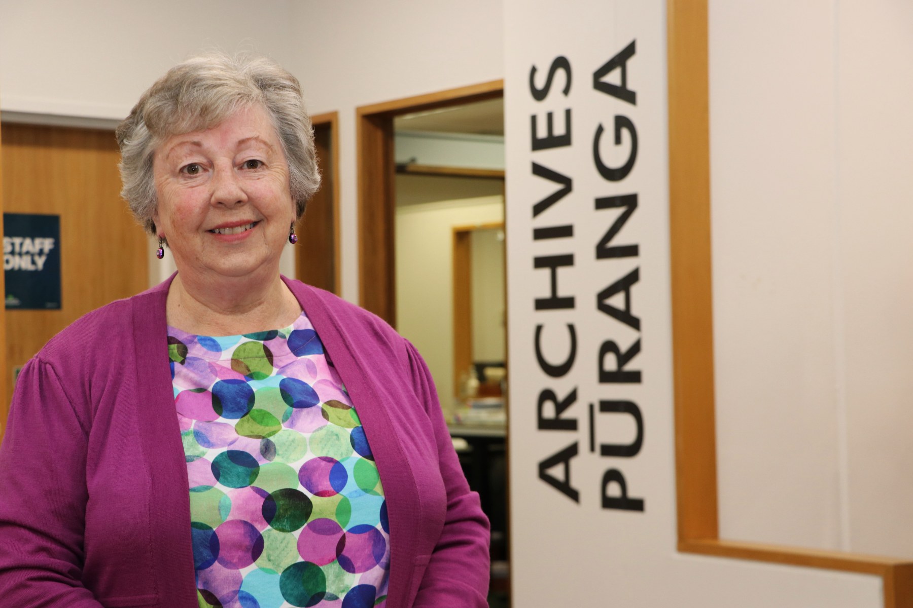 Wendy McArthur stands in front of a sign saying Archives/Pūranga