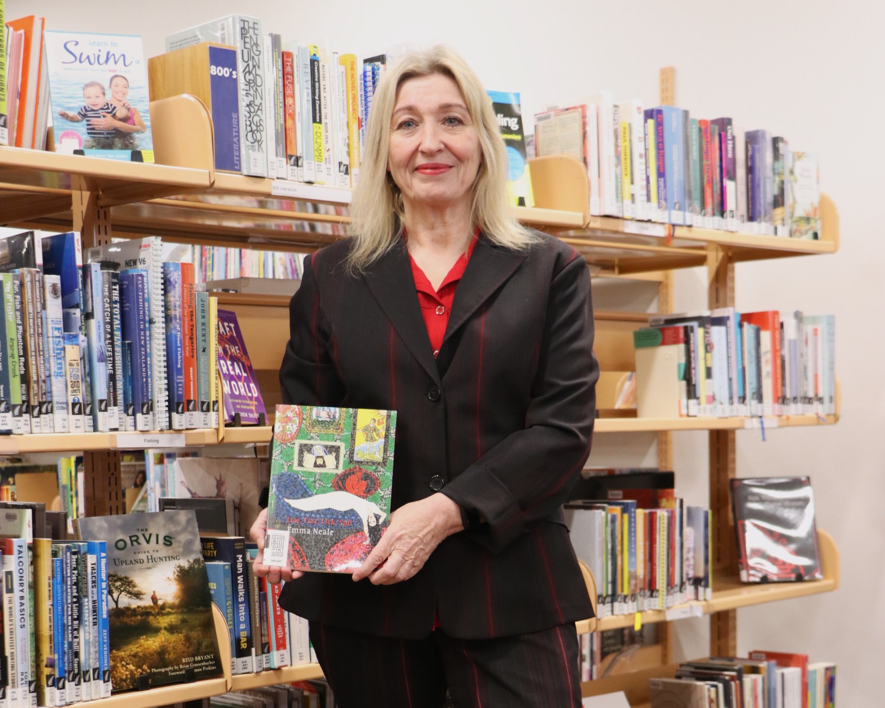 A woman stands in front of a bookshelf holding a poetry book with a colourful cover.