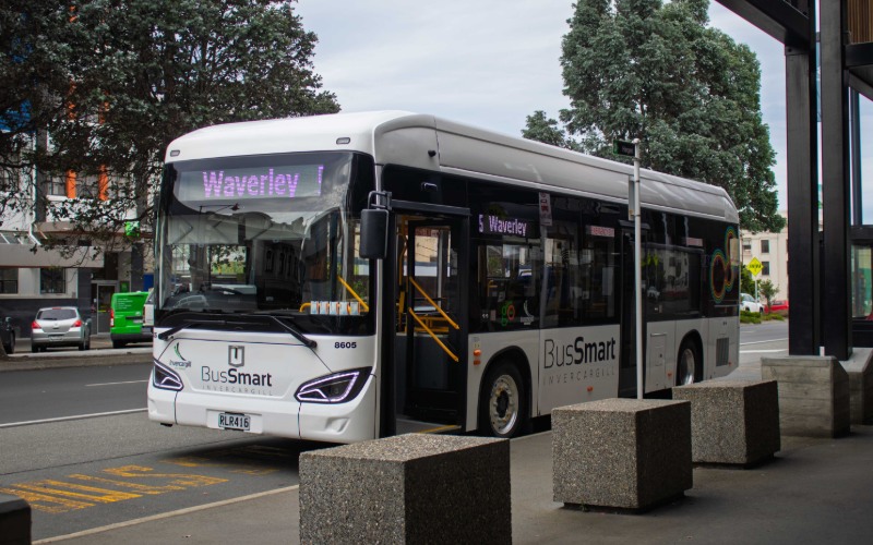 A white bus with black windows sits on the side of a street.