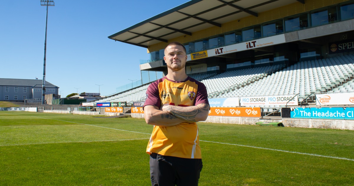 A man standing on a green grassy playing field in front of a grandstand.