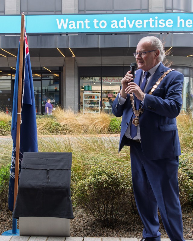 Invercargill Mayor Tom Campbell speaking beside the covered memorial plaque and a New Zealand Police flag.